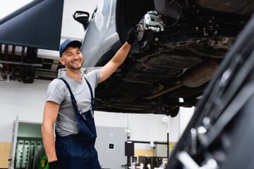 Obraz na płótnie Canvas selective focus of happy mechanic in overalls standing near car