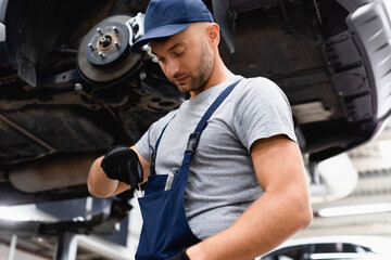 low angle view of mechanic in overalls taking wrench from pocket near car
