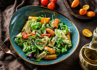 Fresh summer salad with deep-fried cheese sticks, blue cheese, tomatoes, cucumbers, granola, greens and orange in bowl on wooden background. Healthy food, clean eating, Buddha bowl salad, top view