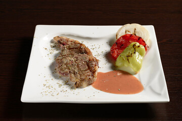 Grilled beef steaks with vegetables of tomato, onion and bell pepper on a square plate on a wooden table. Photos for restaurant and cafe menus