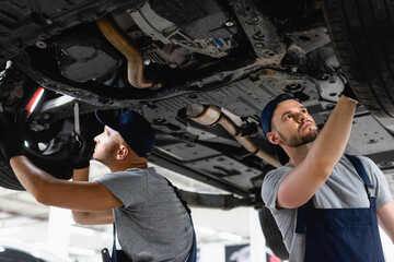 Fototapeta na wymiar low angel view of handsome mechanics in caps fixing car in service station