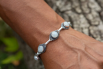 Outdoor closeup of a hand wrist wearing silver metal bracelet with moon stone gem