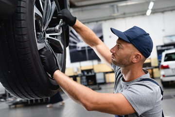 side view of technician in rubber gloves touching wheel disk while repairing car