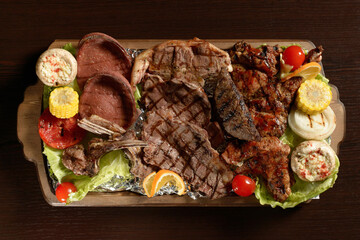 Assortment of grilled meat with vegetables on a rustic tray and wooden table
