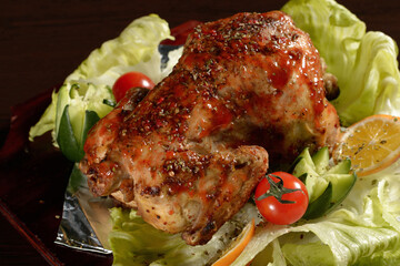 Close up of a whole grilled chicken with vegetables on a wooden table
