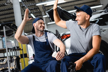 Happy auto mechanic sitting and giving high five to colleague at service station