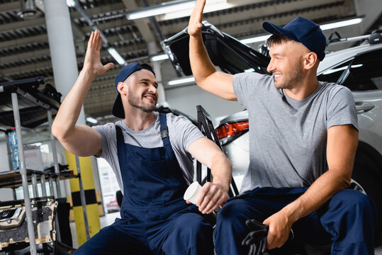 Happy auto mechanic sitting and giving high five to colleague at service station