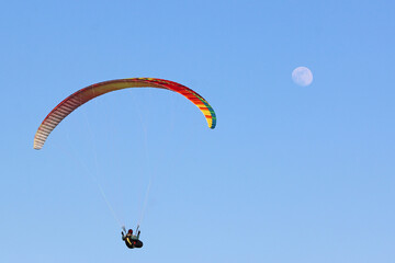Paraglider flying wing in a blue sky with the moon	