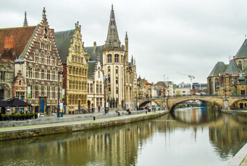 Fototapeta na wymiar Ghent, Belgium; Public buildings and a church line a canal in Ghent. A stone bridge crosses the canal.