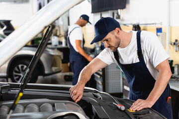 Obraz na płótnie Canvas selective focus of mechanic in cap repairing car near coworker in workshop