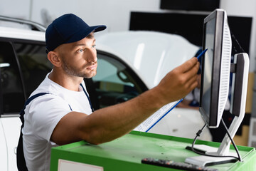 selective focus of mechanic in cap holding pen near computer monitor in workshop