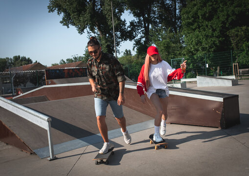 Young couple hangout in skate park having fun driving skateboard.