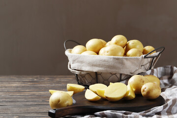 Basket full of fresh, young potatoes board, towel and knife on wooden background, top view