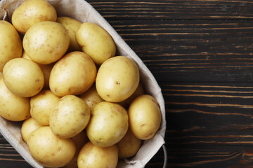 Basket full of fresh, young potatoes board, towel and knife on wooden background, top view