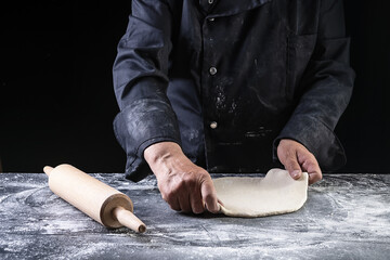 Chef making dough for pizza on dark backrground