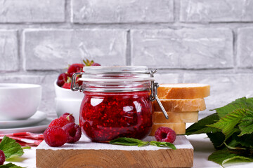 Raspberry jam in glass jar against the grey brick wall