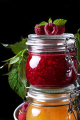 Raspberry and orange jams in glass jars against the black background