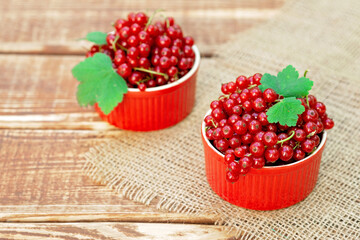 Red currant berries in a cocotte bowl on a wooden background with burlap. Natural vitamins concept.