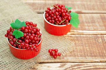 Red currant berries in a cocotte bowl on a wooden background with burlap. Natural vitamins concept.