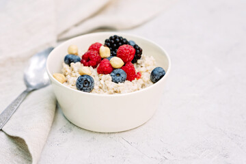 Oatmeal with raspberries, blueberries, blackberries and nuts on a gray concrete background. Healthy healthy breakfast.