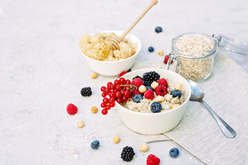 Oatmeal with raspberries, blueberries, blackberries, red currants and nuts on a gray concrete background with honey in a comb. Healthy healthy breakfast.