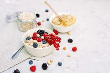 Oatmeal with raspberries, blueberries, blackberries, red currants and nuts on a gray concrete background with honey in a comb. Healthy healthy breakfast.