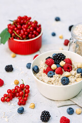 Oatmeal with raspberries, blueberries, blackberries, red currants and nuts on a gray concrete background. Healthy healthy breakfast.