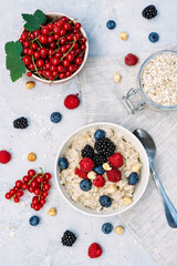 Oatmeal with raspberries, blueberries, blackberries, red currants and nuts on a gray concrete background. Healthy healthy breakfast. Flat lay