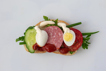 On the table is an appetizing sandwich with sausage, eggs, cucumber. The sandwich is watered with ketchuk and mayonnaise. The sandwich is tasty but not healthy