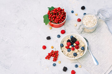 Oatmeal with raspberries, blueberries, blackberries, red currants and nuts on a gray concrete background. Healthy healthy breakfast.