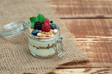 Muesli granola with yogurt and fresh raspberries, blueberries and blackberries, nuts in a glass jar on a wooden background. Healthy and healthy breakfast.