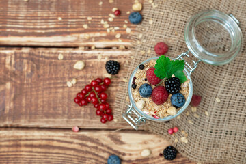 Muesli granola with yogurt and fresh red currant berries raspberries blueberries and blackberries, nuts in a glass jar on a wooden background. Healthy breakfast.