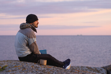 A man with a book on the background of the sea. The background is blurred.