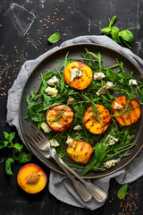 Close-up diet salad grilled peach, arugula and blue cheese in a plate on a black stone background. Top view, flat lay.
