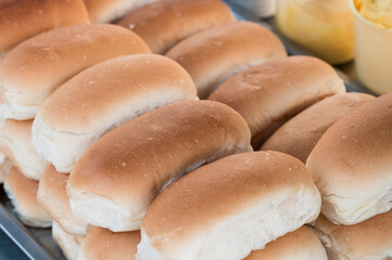 Many round soft buns on a table with a bucket of butter