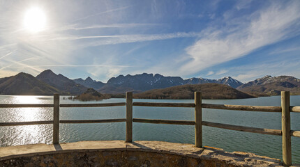 Mountain tourist viewpoint in front of a reservoir or swamp, with a wooden railing and the sun in the sky