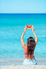 Happy girl having fun on the beach and eating watermelon