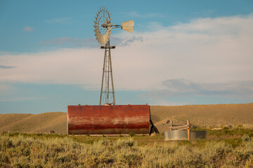 Rural metal windmill and stock tank with foreground sagebrush.
