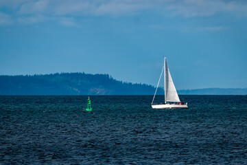 Obraz premium Isolated sailboat profile with blue sky background and green bouy