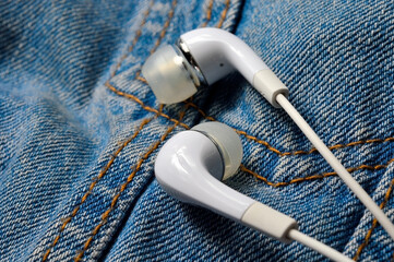 white headphones for the phone on the background of a denim jacket. close-up.