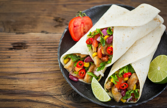 Fresh tortilla wraps with chicken meat and vegetables on the wooden table