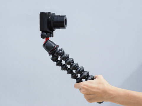 Female hand holds tripod with compact digital camera. Blogger concept.