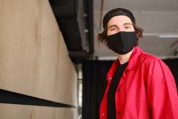 Portrait of a young man 25-30 years old in a black protective mask, black cap and red jacket. 