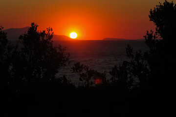 Sunset behind the mountains at the bottom of the Mediterranean sea with silhouettes of trees, commune of Sorrento, province of Naples, Italy