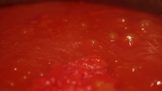 Tomato sauce bubbling in stainless steel pan over electric stove, super close up