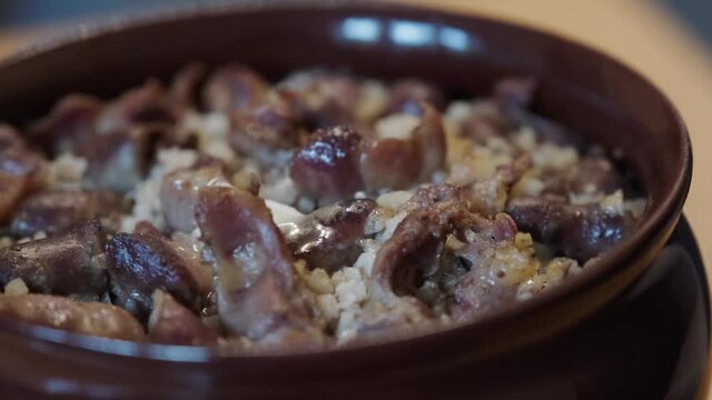 Hot barley porridge with chicken offal in a brown clay pot. a dish of chicken giblets and porridge.