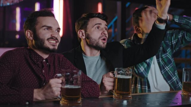 Happy friends in a pub while drinking some beer concentrated watching a football match they screaming and gesticulating with hands while watching on tv