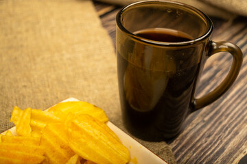 Potato chips with cheese sauce and a coffee mug on a wooden background. Close up.