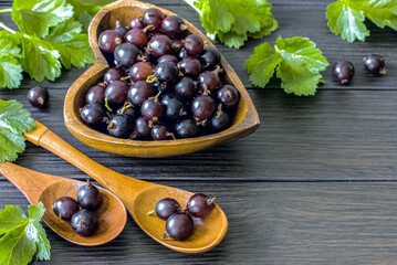 ripe red gooseberries in a wooden bowl and spoons on a wooden background close-up. background with fresh gooseberry berries in a bowl and green leaves above.