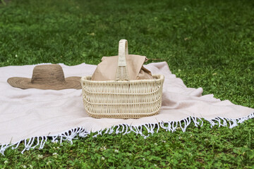 Picnic on a blanket on the grass. Wicker basket with food in a paper bag and hat.